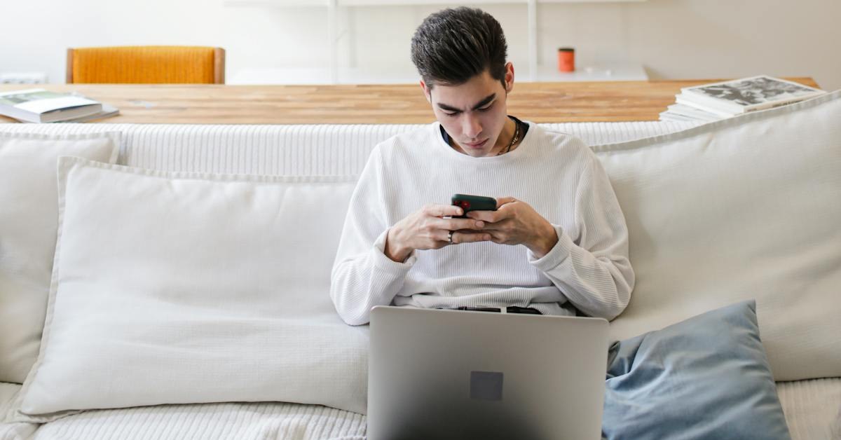 Young professional with laptop open but engaged with short-form video on his smartphone instead